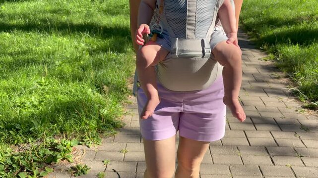 Mother carries baby. a baby secured in a beige mesh ergonomic carrier.