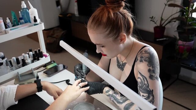 Nail technician works on a client's fingernails using an electric nail drill at a manicure table. Professional nail care, beauty treatment and salon service concept