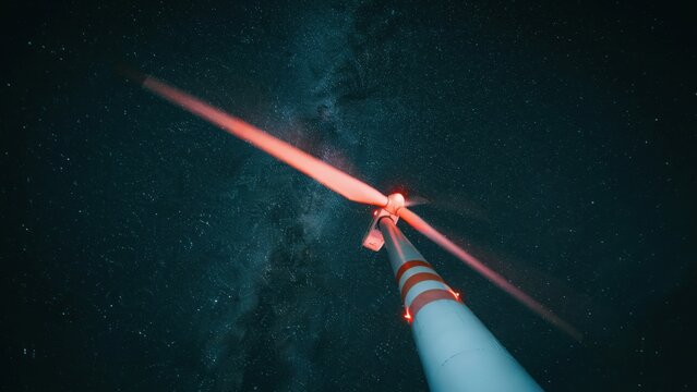 Low angle view of a single modern wind turbine at night against a dark sky filled with stars renewable generation