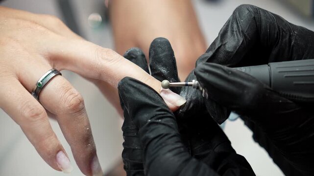 Nail technician removes cuticle with a ball drill bit and cleans the fingernail with a brush. Professional manicure, cuticle care and beauty salon service concept