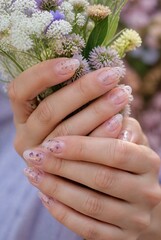 Fototapeta premium Woman Hands Holding Wildflower Bouquet with Glitter Nail Art in Soft Natural Light