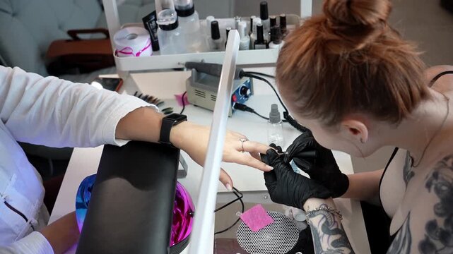 Nail technician applies a base coat to a client's fingernails at a manicure table. Professional manicure, nail care and beauty salon service concept