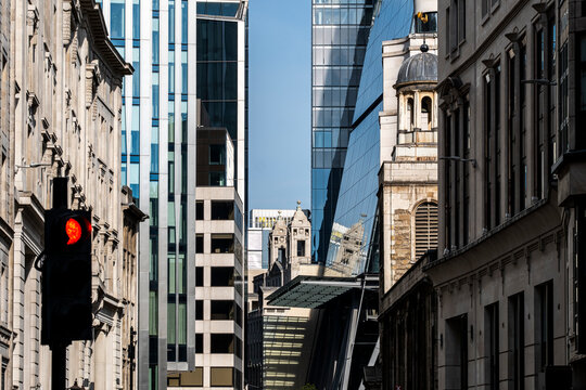 Historic stone and modern glass rise behind a red traffic signal as buildings along a street in London, England, create facade contrast within urban architecture.