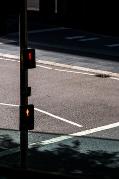 Light and shadow divide empty asphalt around two pedestrian signals, while traffic control marks the road and crossing on a quiet urban street in London, England.