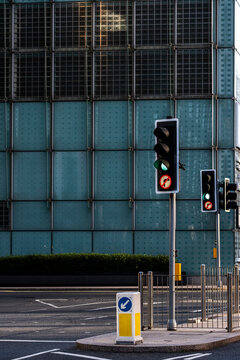 Against a gridded building facade, small lights regulate a quiet junction as traffic signals face a street in London, England, amid dense urban architecture.