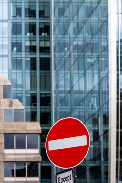 A red sign interrupts the street view in London, England, set against glass office towers whose facade and urban architecture frame the traffic scene.