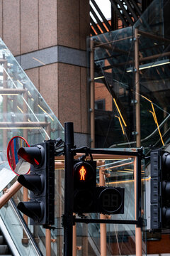 A pedestrian signal glows red over a crossing as glass office walls catch light, while traffic moves along a street in London, England, through urban architecture.