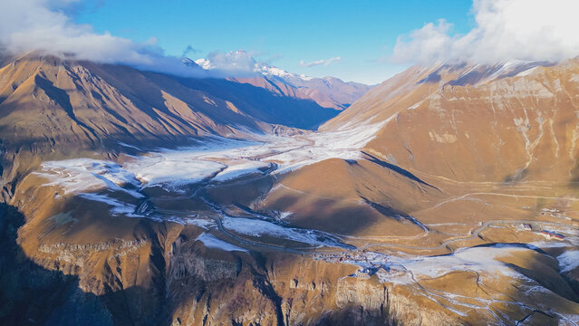 Aerial wide view of Gudauri Russia Georgia Friendship Monument on cliff edge with snow covered Caucasus mountain ranges and Kazbegi peak under blue sky Georgia