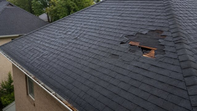 Aerial view of localized wind damage and missing shingles on a suburban roof for home insurance claim assessment and repair advertising