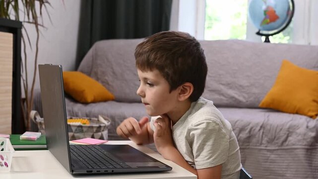 6 year-old boy sitting in living room, learning to type on notebook doing homework. Young child focused on computer screen, Elementary school student studying independently indoors, at home