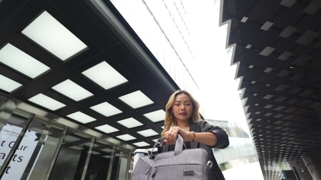 Businesswoman standing in a modern urban setting, holding her bag with a confident expression, representing professionalism, elegance, and readiness in a sleek and dynamic environment.