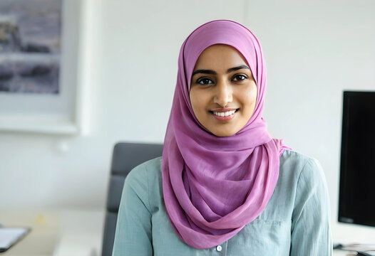 Smiling young muslim woman wearing a purple hijab and light green shirt in a modern office setting, this professional female is seated in a modern office environment, confidence and happiness