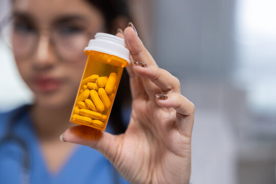 Pill bottle medicine tablet doctor hand woman clinic prescription health female medical worker holding orange pill bottle with yellow tablet clinical setting, focused hand, blurred face background