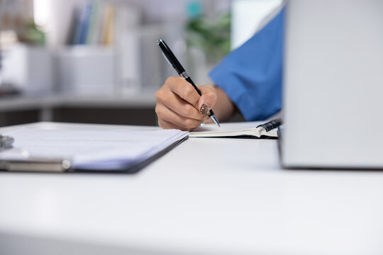 Hand pen notebook writing desk office laptop document clipboard workplace closeup of person taking note on paper with calm focused mood