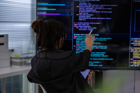Programmer code screen technology woman office software developer data monitor, woman programmer reviewing code large monitor modern office, holding tablet with focused posture near digital