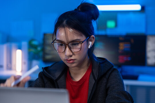 Young woman eyeglass earbud laptop office technology night concentration Asian worker Young woman with eyeglass and earbud using laptop blue office night, focused Asian worker modern technology