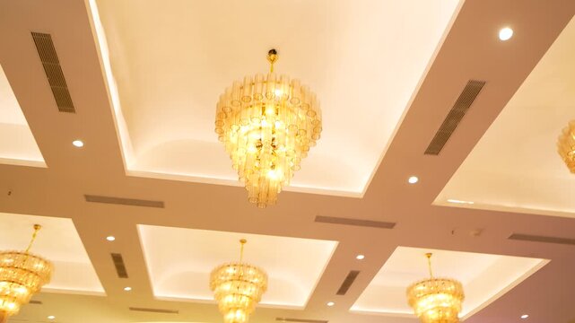 Luxury crystal chandeliers hanging from a modern false ceiling in a banquet hall interior.