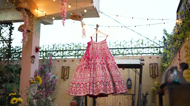 Indian bride in red floral lehenga under wedding mandap with hanging decor and guests seated