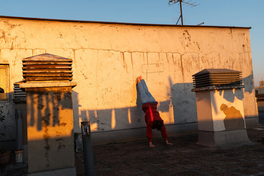 Young Woman Practicing Handstand On Rooftop At Sunset