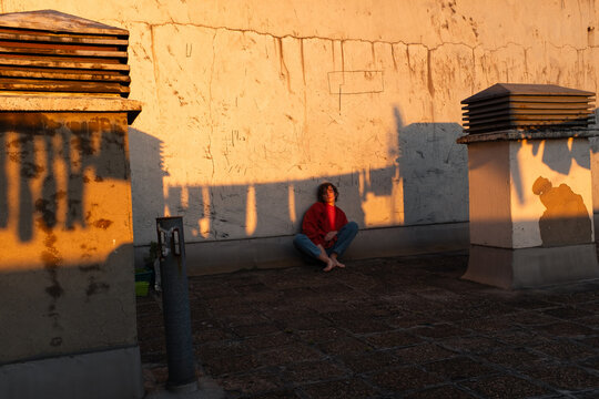 Young Woman Sitting Alone On Rooftop At Sunset