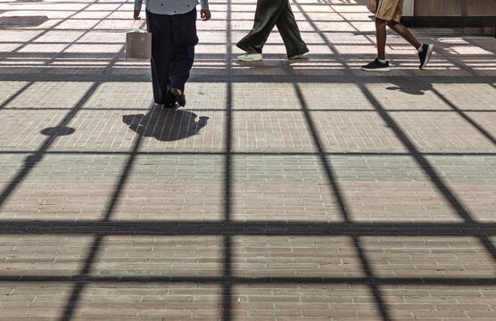 Pedestrians Walking Across Sunlit Grid Shadows on Brick Floor