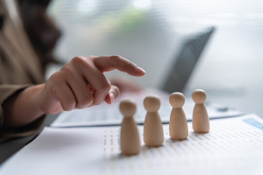 Recruiter selecting wooden people figures during candidate evaluation, representing human resources, hiring decisions, talent recruitment, employee screening, workforce planning and selection.