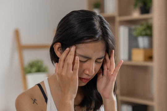 Woman headache temple pain stress fatigue migraine discomfort indoor home, holding temples with eyes closed in room, showing tired expression during health problem