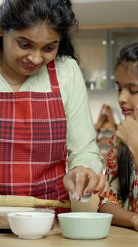 Indian Asian mother happily teaches her small daughter how to make roti or chapati, showcasing their skills with joy as they smile at the camera