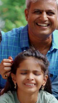 An Indian Asian family of four joyfully celebrates their small daughter's birthday by cutting a cake adorned with candles, surrounded by glitter, love, and laughter as they pose for a memorable photo