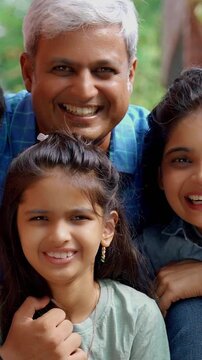 An Indian Asian father in his late forties playfully encourages his small daughter to drink milk while she sits happily on the kitchen platform, creating a joyful moment filled with love and laughter