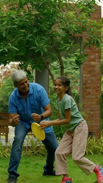 Indian Asian family of four spending quality time outdoors in their home lawn, parents in their forties watching as teenage son teaches his little sister how to throw a frisbee or flying disc