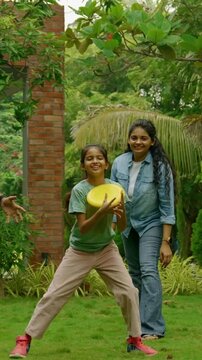 Indian Asian family of four spending quality time outdoors in their home lawn, parents in their forties watching as teenage son teaches his little sister how to throw a frisbee or flying disc