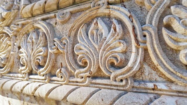 Closeup of weathered ornate stone carving with swirling floral pattern on historic building.
