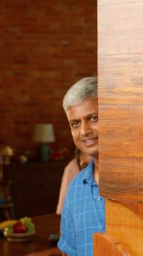 Indian Asian family of four joyfully welcomes guests to their home, as parents in their forties and their teenage son and small daughter open the big wooden entrance door with warm smiles
