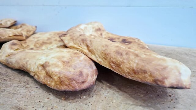 Freshly baked traditional georgian flatbread pieces rest on rustic wooden table surface.