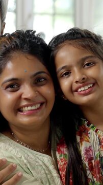 Indian Asian family of four, parents in their forties, sitting closely on a sofa with their two kids, smiling warmly while looking at the camera, capturing a joyful moment together indoors