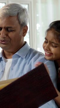 A closeup of a happy Indian Asian family consisting of parents in their mid-forties, a teenage son, and a small daughter joyfully reminiscing together while flipping through a cherished photo album