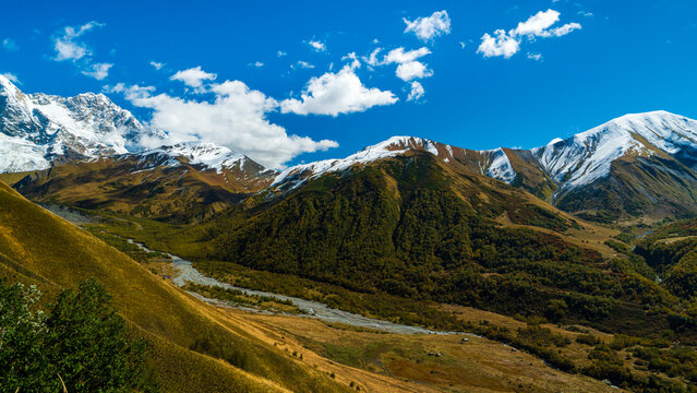 Landscape photograph of snow covered mountains and glacier river valley viewed from Chkhutnieri pass in Svaneti Georgia.