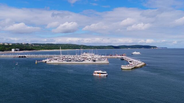Aerial video showing the pier and marina filled with moored boats in Sopot, Poland, featuring coastline, water, and moving vessels.