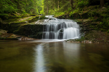 Fototapeta premium Small waterfall on the river flowing through a lush forest in the Jizera Mountains, Czech Republic, captured with a long exposure creating silky smooth water.