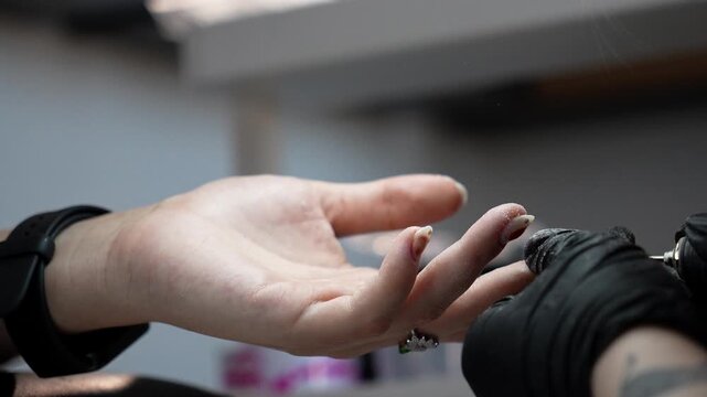 Nail technician removes excess material from the underside of a shaped nail using an electric drill. Professional finishing and precise nail shaping concept