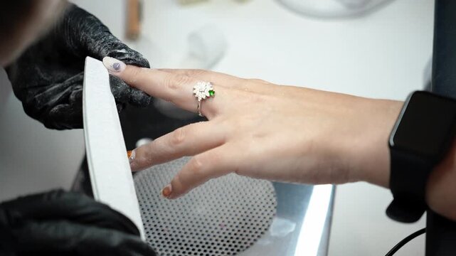 Nail technician files the edges of the nails during the final stage of a manicure. Professional finishing, nail shaping and beauty care concept