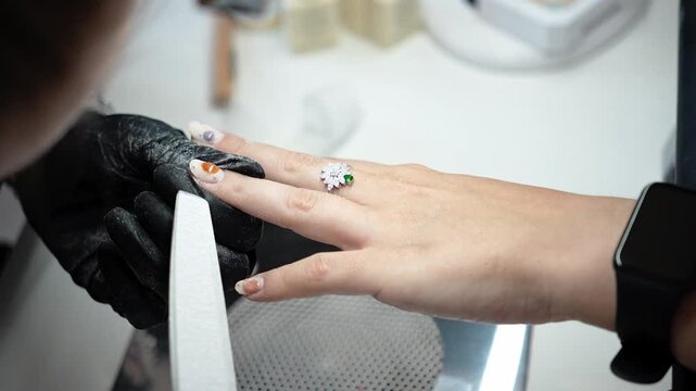 Nail technician files the edges of the nails during the final stage of a manicure. Professional finishing, nail shaping and beauty care concept
