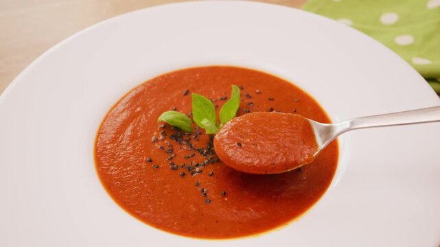 Close up shot of hand dipping spoon into bowl of creamy tomato and red pepper soup. Tasting rich homemade vegetable cream soup.