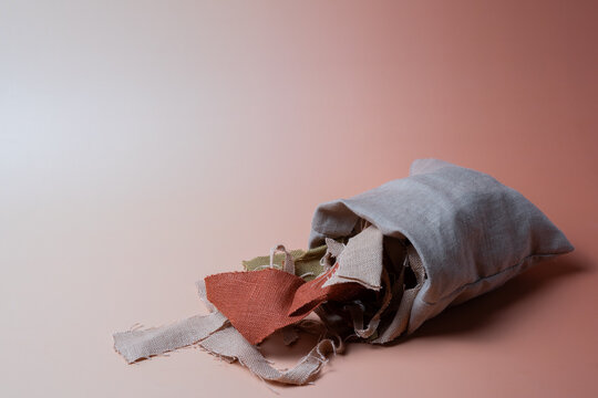 Fabric scraps in linen bag on pink background with copy space, sustainable textile recycling concept