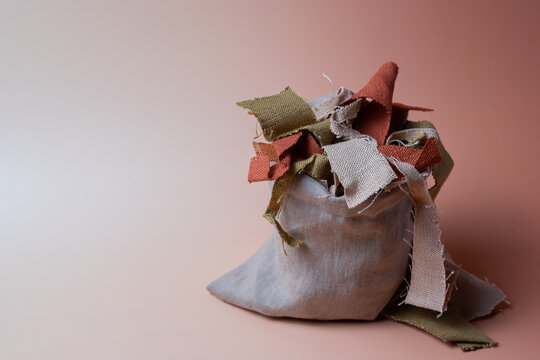 Fabric scraps in linen bag on pink background with copy space, sustainable textile recycling concept