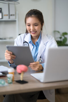 Young Asian female doctor smiling while reviewing patient records on digital tablet in modern clinic office