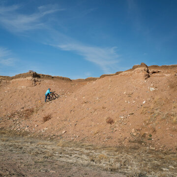 male cyclist is walking a gravel bike uphill on a cliff in Colorado prairie - Soapstone Prairie Natural Area