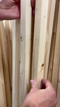 a man's hands carefully inspecting and selecting light-colored wooden planks in a hardware store or lumber yard. Hardware store