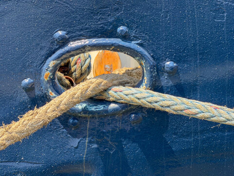 Thick mooring rope threaded through hawsehole of blue ship hull docked at cruise terminal in Antwerpen, Belgi&euml;